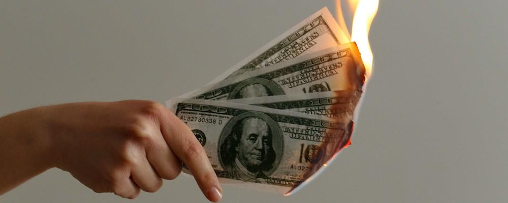 Hand holding 100 dollar bills that are on fire