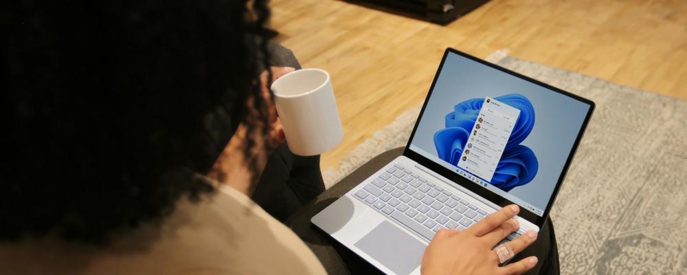 overhead photo of a person typing on a windows 11 laptop and holding coffee mug