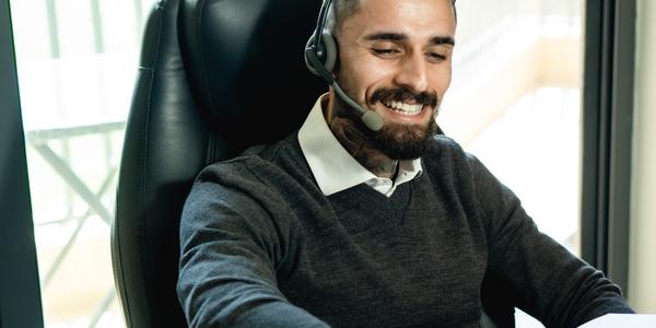 person smiling and wearing a headset and looking at a computer