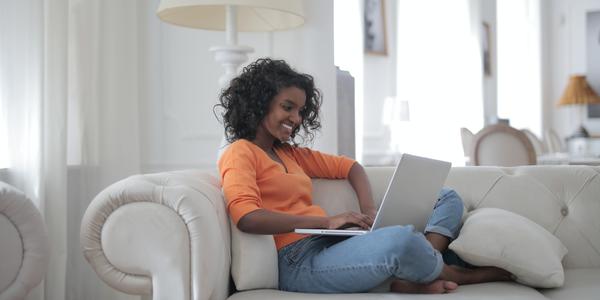 Woman sitting on a white couch smiling while holding a laptop
