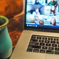 Photo of a laptop with video conference on screen and a coffee mug in the foreground